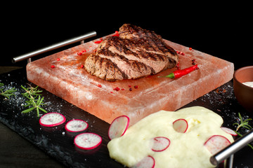 Pieces of roast beef with spices served on black slate.