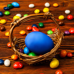 A basket of delicious Easter eggs and sweets on wooden background