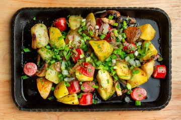 Fried potatoes with mushroom and sausage in cast iron frying pan.