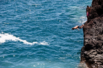 Junge springt von einer Klippe ins Meer