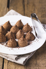 Homemade Chocolate Truffles With Cocoa Powder on a White Plate Old Wooden Background Tasty Candy Vertical