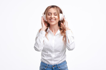 Wireless connection. Portrait of young beautiful woman posing isolated over white background listening music with headphones. 