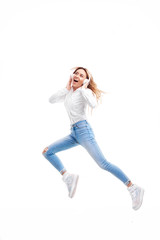 Gorgeous redhead lady listening music on radio in headphones and jumping high. Charming girl in in casual clothes and earphones dancing with hair waving on white background. Full-length portrait
