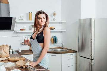 Sexy woman in underwear and blue apron holding eggs in kitchen
