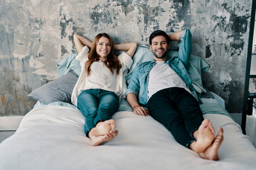 Perfect couple. Beautiful young couple looking at camera and smiling while spending time in bed at home