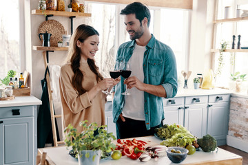 Cheers! Beautiful young couple cooking dinner and drinking wine while standing in the kitchen at home
