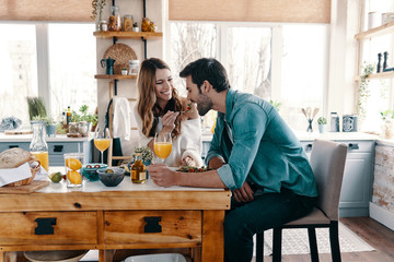 Try it! Beautiful young couple enjoying healthy breakfast while sitting in the kitchen at home - obrazy, fototapety, plakaty