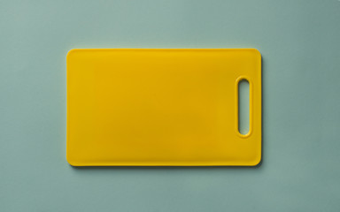 Colored yellow plastic cutting board on blue background, top view.