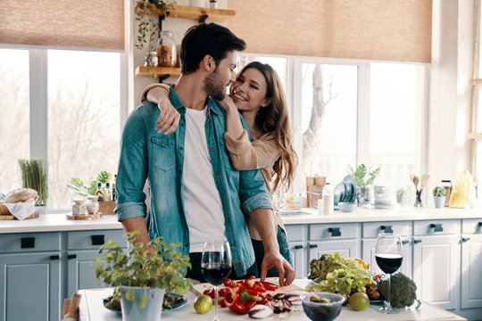 Enjoying Time Together. Beautiful Young Couple Cooking Dinner While Standing In The Kitchen At Home