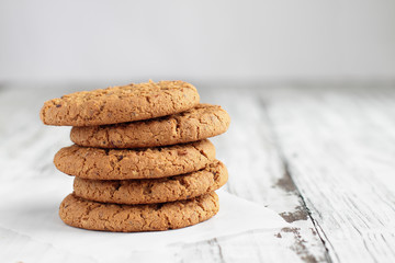 Stack of fresh homemade oatmeal cookies with a bottle of milk on a white table against a white background.