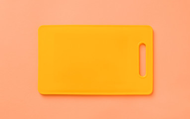 Colored yellow plastic cutting board on orange background, top view.