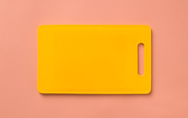 Colored yellow plastic cutting board on pink background, top view.