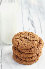 Overhead shot of stack of fresh homemade oatmeal cookies with a bottle of milk on a white table against a white background..