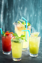 Three glasses of lemonades with lemon and strawberry and a pitcher on textured wooden background. Copy space available.