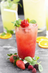 Iced tea with strawberries and mint. Glass of lemonade and a lemonade jar at the background out of focus.