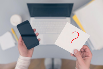 Woman clerk sitting at the office table and holding note sticker with question mark. Concept.