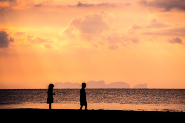 Fototapeta premium Children playing on the beach at the sunset. Silhouette child and tropical sky in summer season