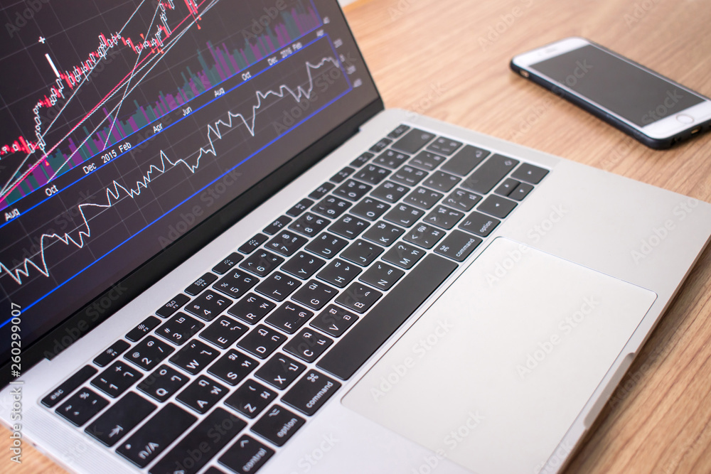 Poster the close-up image of the laptop shows the financial graph data on the wooden table with the smartph