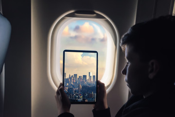 Caucasian boy using tablet pc taking picture through airplane window  New york city with skyscrapers. USA