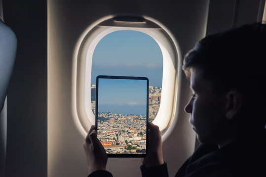 Caucasian boy using tablet pc taking picture through airplane window San Francisco cityscape. California. USA