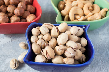 colorful bowls with mixed nuts on a gray background. Walnut, pistachios, almonds, hazelnuts and cashews, walnut.