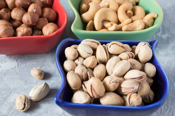 colorful bowls with mixed nuts on a gray background. Walnut, pistachios, almonds, hazelnuts and cashews, walnut.