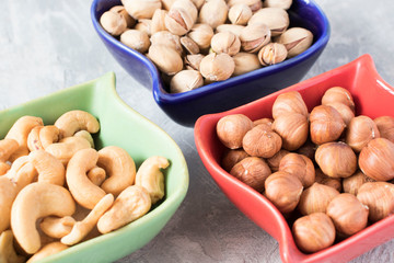 colorful bowls with mixed nuts on a gray background. Walnut, pistachios, almonds, hazelnuts and cashews, walnut.