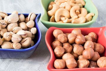 colorful bowls with mixed nuts on a gray background. Walnut, pistachios, almonds, hazelnuts and cashews, walnut.