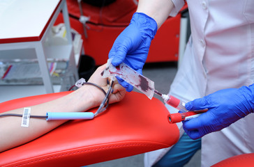 Nurse taking blood from the vain of a donor - hypodermic needle, tubes, container with blood