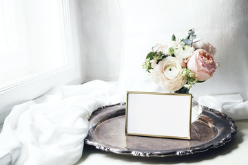 Spring, summer still life. Blank golden photo frame mockup on old silver tray near window. Vintage...