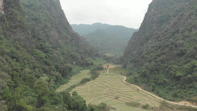 Aerial: flying over scenic cliffs rock pinnacles tropical jungle rice paddies valley stunning landscape around Vang Vieng popular destination in Laos Asia. Native cinelike D-log color profile