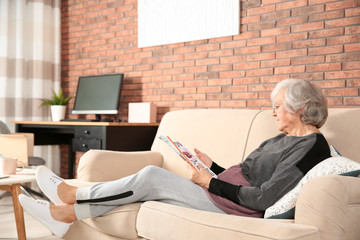 Fototapeta na wymiar Elderly woman with magazine on sofa in living room