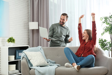 Emotional young couple with laptop celebrating victory at home