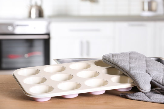 Clean baking dish, muffin pan and oven glove on table in kitchen. Space for text