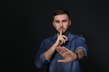 Man showing HUSH gesture in sign language on black background