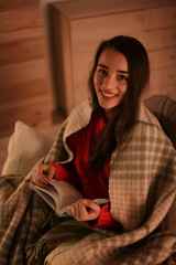 Woman with plaid reading book at home. Winter season
