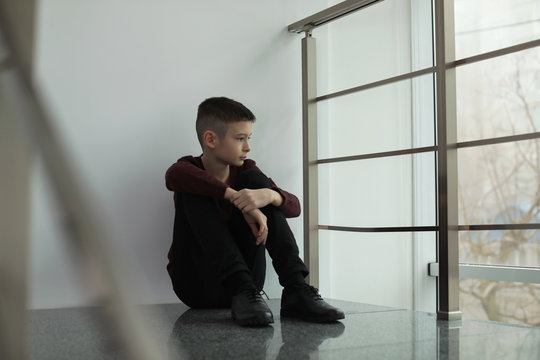 Upset preteen boy sitting on staircase indoors - Powered by Adobe