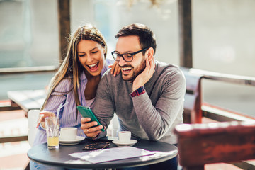 Young cheerful man and woman dating and spending time together in cafe, using phone.