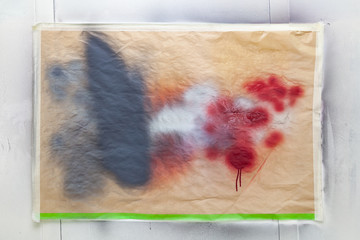 A sheet of paper attached to the wall with scotch tape stains from splashing paint to test color before painting