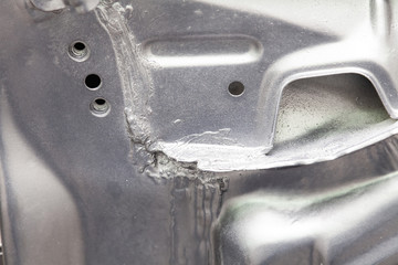 Close-up on the weld connecting the metallic parts of a car of silver color smeared with sealant and painted. Metalworking industry.