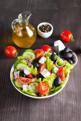 Fresh Greek salad made of cherry tomato, ruccola, arugula, feta, olives, cucumbers, onion and spices. Caesar salad in a white bowl on wooden background. Healthy organic diet food concept.
