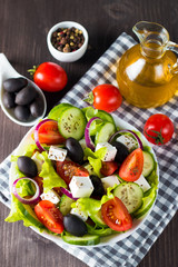 Fresh Greek salad made of cherry tomato, ruccola, arugula, feta, olives, cucumbers, onion and spices. Caesar salad in a white bowl on wooden background. Healthy organic diet food concept.