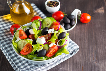 Fresh Greek salad made of cherry tomato, ruccola, arugula, feta, olives, cucumbers, onion and spices. Caesar salad in a white bowl on wooden background. Healthy organic diet food concept.