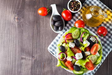 Fresh Greek salad made of cherry tomato, ruccola, arugula, feta, olives, cucumbers, onion and spices. Caesar salad in a white bowl on wooden background. Healthy organic diet food concept.