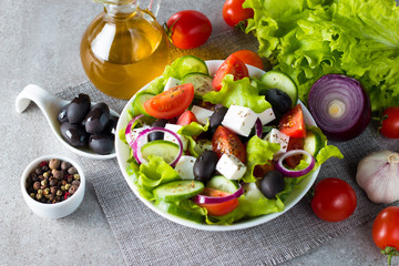 Fresh Greek salad made of cherry tomato, ruccola, arugula, feta, olives, cucumbers, onion and spices. Caesar salad in a white bowl on wooden background. Healthy organic diet food concept.