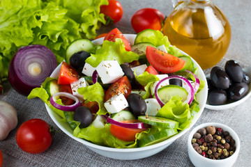 Fresh Greek salad made of cherry tomato, ruccola, arugula, feta, olives, cucumbers, onion and spices. Caesar salad in a white bowl on wooden background. Healthy organic diet food concept.