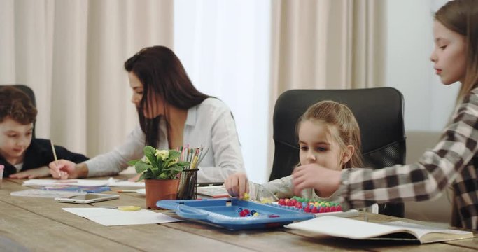 A big family with three kids and a beautiful mature mother spending a time together on the a large kitchen table painting and have a table games background grandmother reading a book. 4k