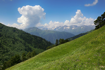Beautiful nature in Russia, the Caucasus. Green hills in the valley, snow-capped mountains in the distance and clouds in the sky
