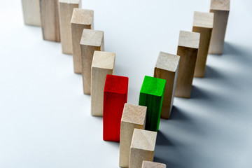 The long curved line of wooden cubes is divided into two after the red and green cubes, as a symbol of a queue, a competition for a position or a turning point, on an uneven white background
