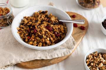 Bowl of homemade granola with nuts and fruits on white linen background. Side view